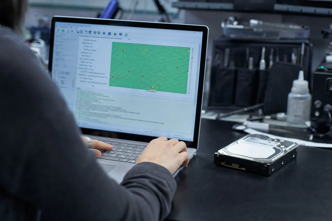 A failing 3.5-inch hard drive beside a laptop running a free DIY recovery check tool