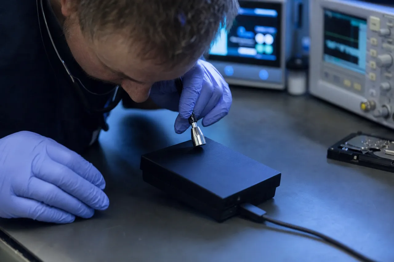 A technician listening closely to a beeping external hard drive connected by USB on the bench, assessing the audible mechanical fault before any further power-on