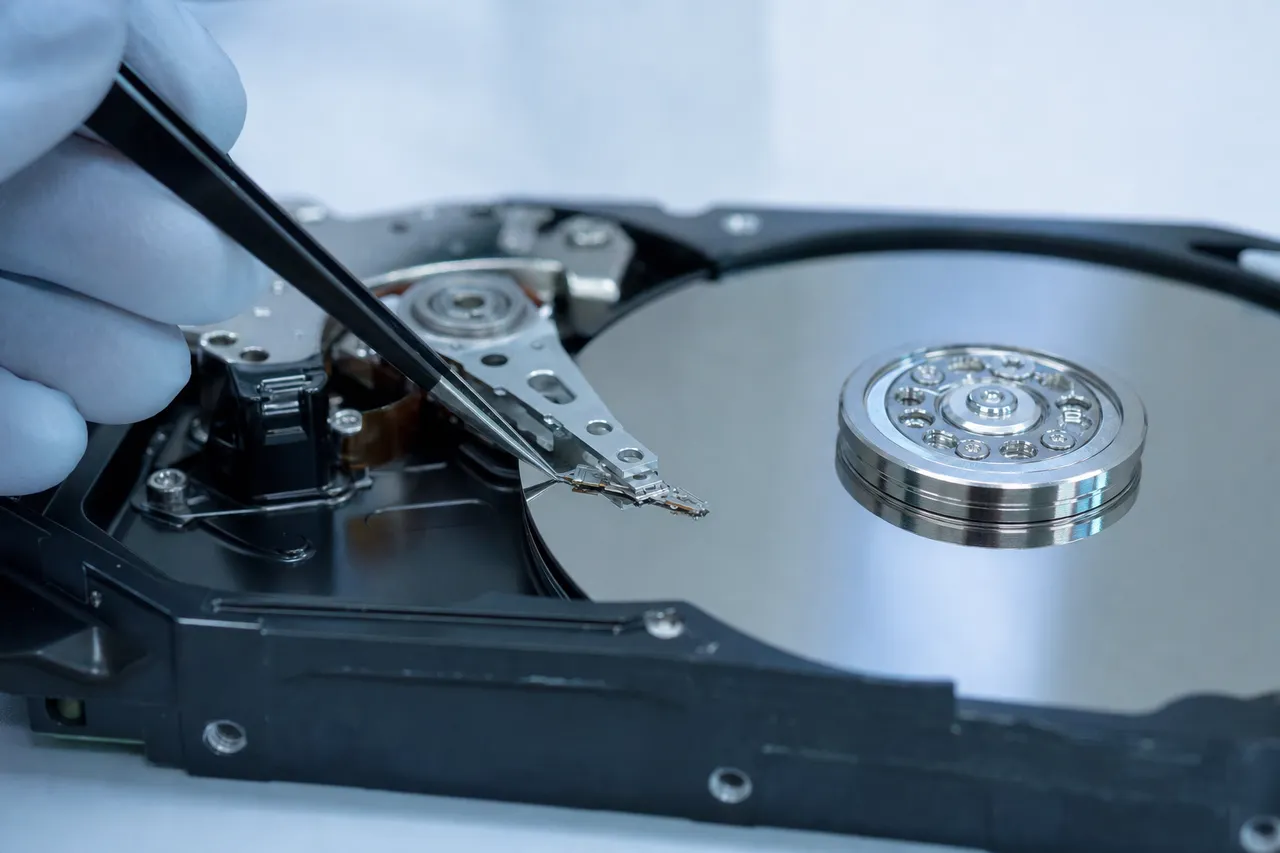 A clean room head stack replacement on an open hard drive, the donor head comb being lowered onto the platters with a specialized tool