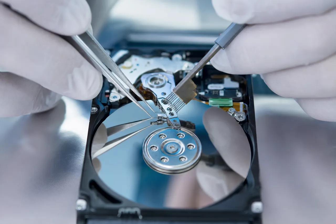 Extreme close-up of a technician using a head comb tool to lift the read/write head stack off the mirrored platters of an opened Hitachi laptop drive
