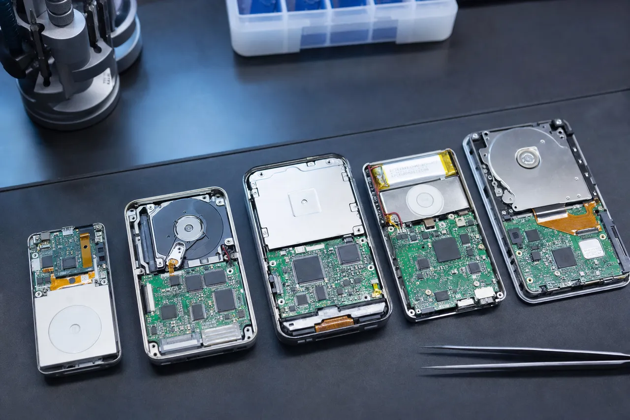 Several disassembled vintage portable music players on a lab mat, some opened to show a tiny 1.8-inch mechanical hard drive and others showing a small circuit board with soldered NAND flash chips.