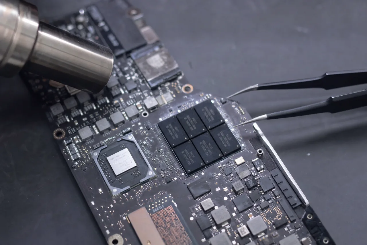 Macro of an Apple MacBook logic board under a stereo microscope showing soldered BGA storage chips and the security controller, with micro-soldering tools nearby.