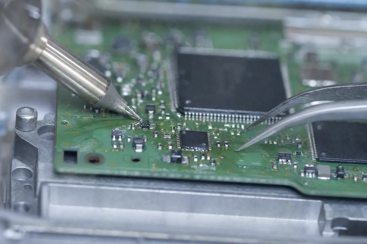 Extreme macro of the green circuit board from a hard drive with a fine micro-soldering iron and tweezers lifting a tiny surface-mount component, solder flux glistening.
