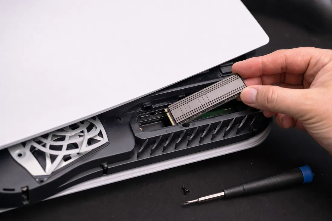 An M.2 NVMe SSD with a heatsink being installed into the expansion storage slot of a modern game console