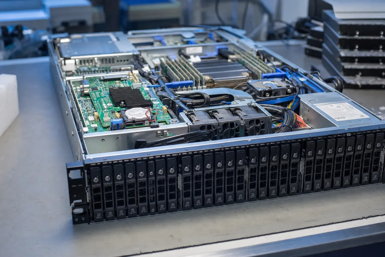 A rackmount enterprise server open on a lab bench with its row of hot-swap SAS drive caddies exposed and a dedicated hardware RAID controller card with a battery-backup cache module visible on the motherboard