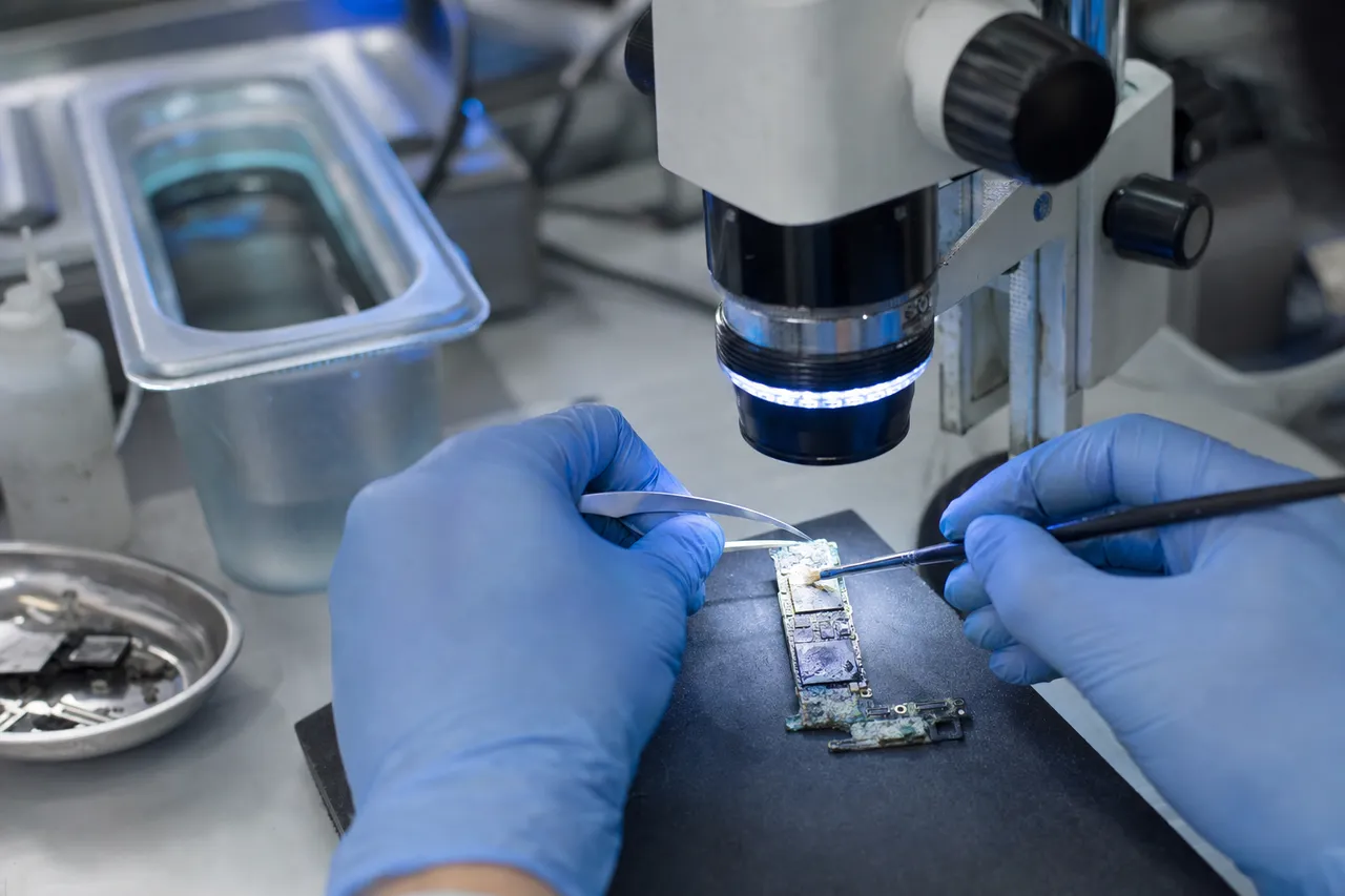 A water-damaged phone logic board with visible corrosion being cleaned under a microscope, an ultrasonic cleaning tank in the background