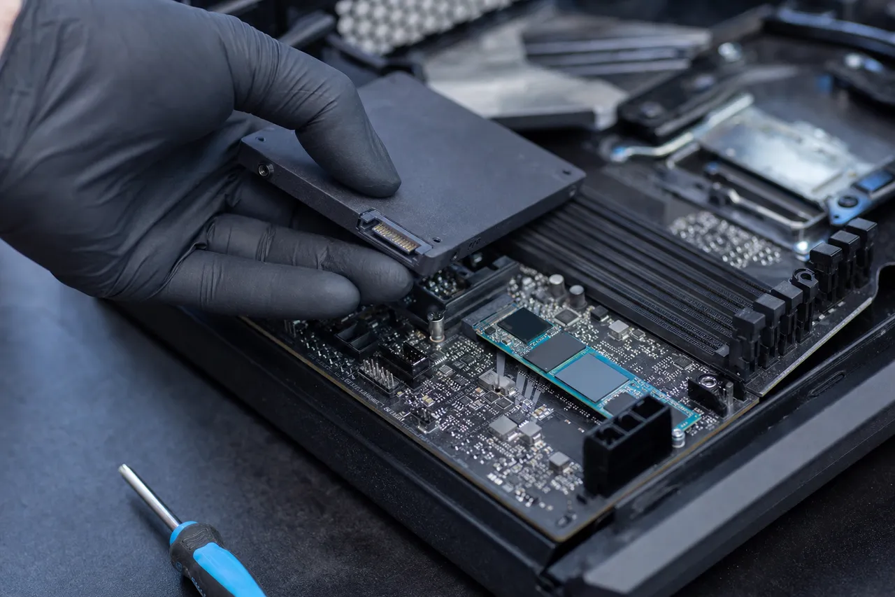 A gloved hand installing an SSD and an NVMe drive into a desktop PC on a repair bench