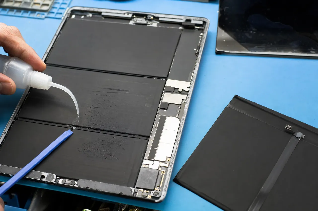 An opened tablet on a repair bench with the display removed exposing the wide flat internal battery and the logic board