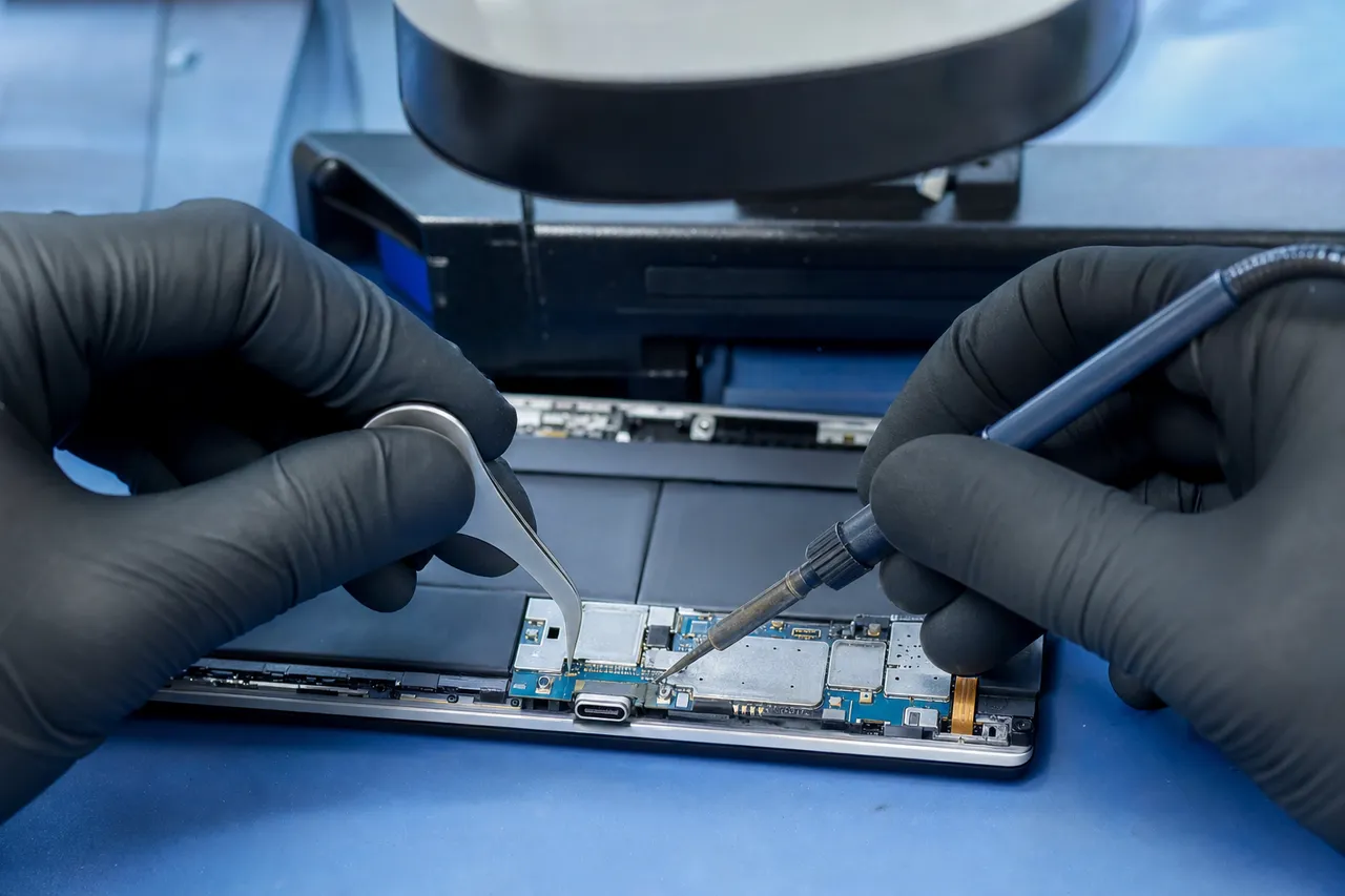Extreme macro close-up of a tablet charging port flex cable being micro-soldered under a stereo microscope on a repair bench
