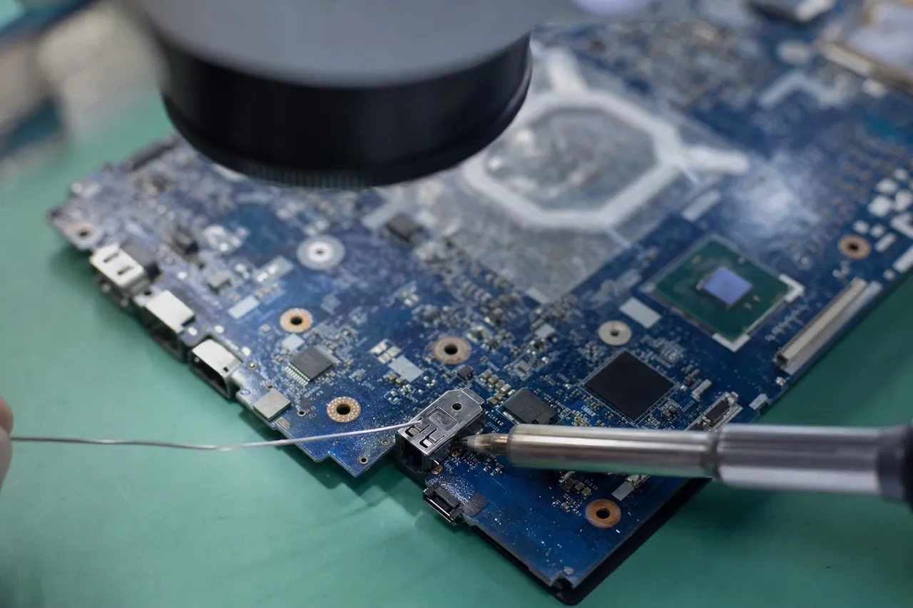 Close macro of a laptop motherboard under a microscope with a soldering iron reflowing the DC charging power jack connector