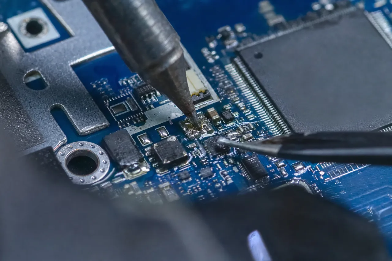 Extreme close-up of micro-soldering on a MacBook logic board under a microscope with a fine soldering iron tip