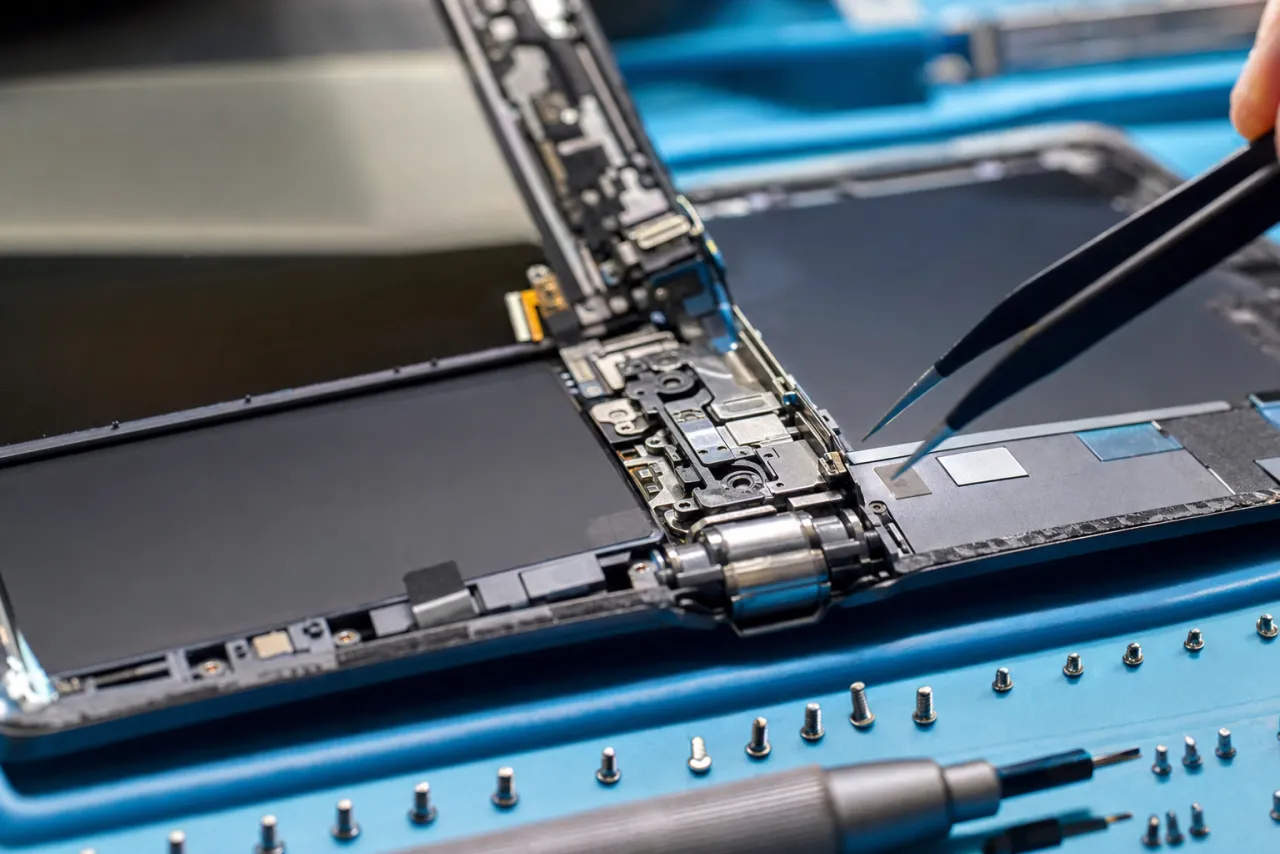 A half-disassembled Galaxy foldable on a repair bench showing the metal hinge mechanism and exposed internals being inspected