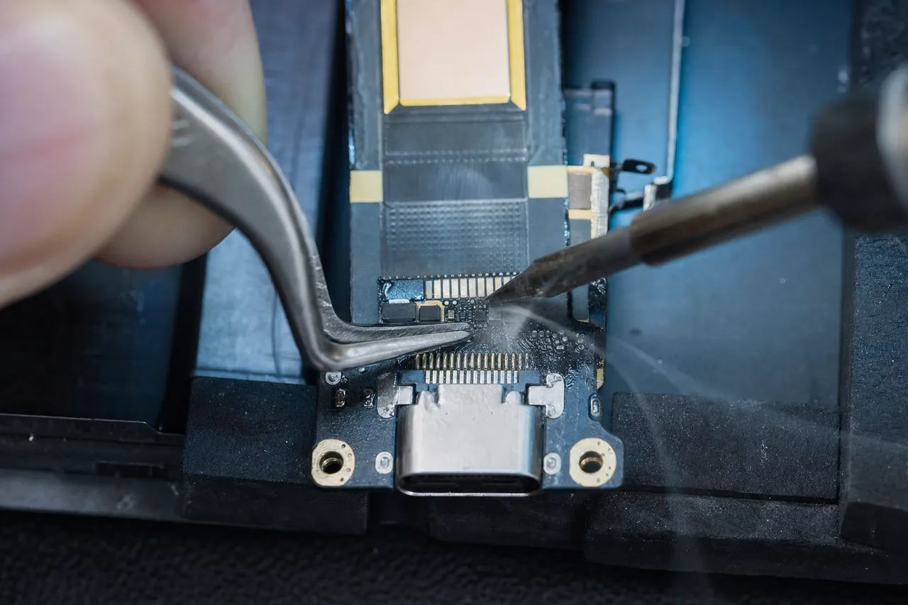 Extreme macro of a tablet USB-C charging port flex being soldered under a microscope on a micro-soldering bench