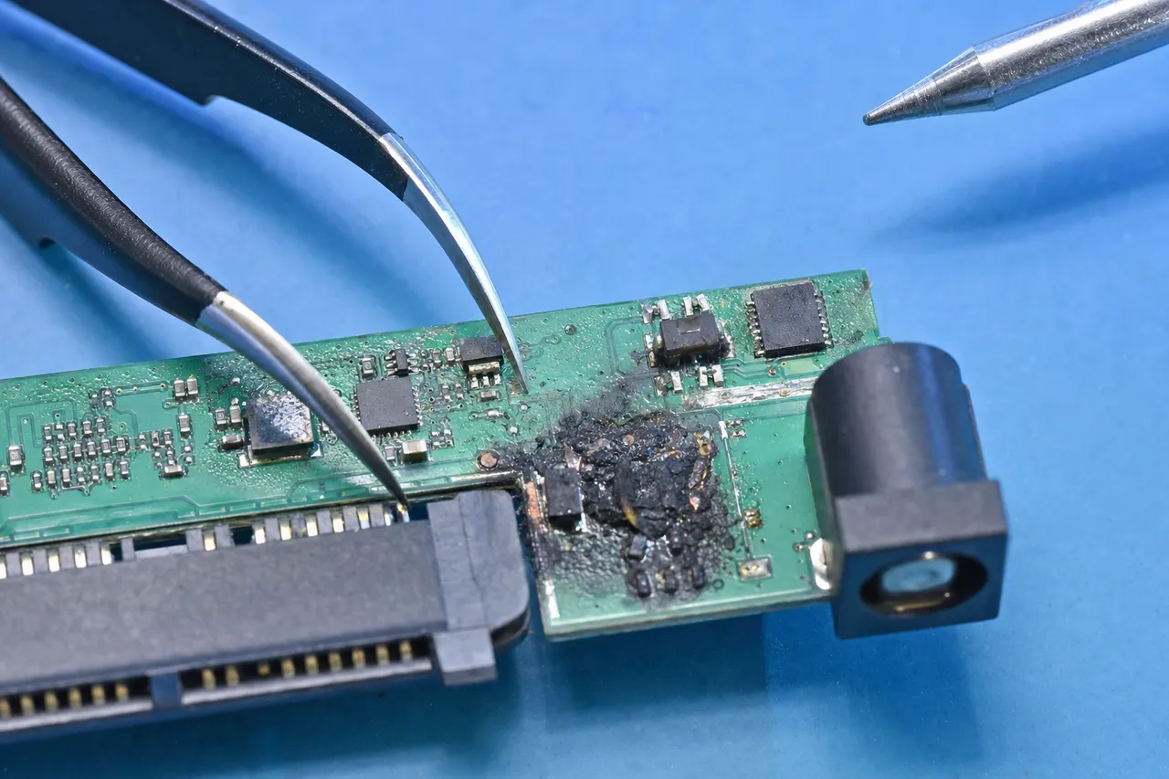 Extreme macro of a surge-damaged WD My Book bridge board with a scorched component and the 12V DC barrel power jack on the recovery bench